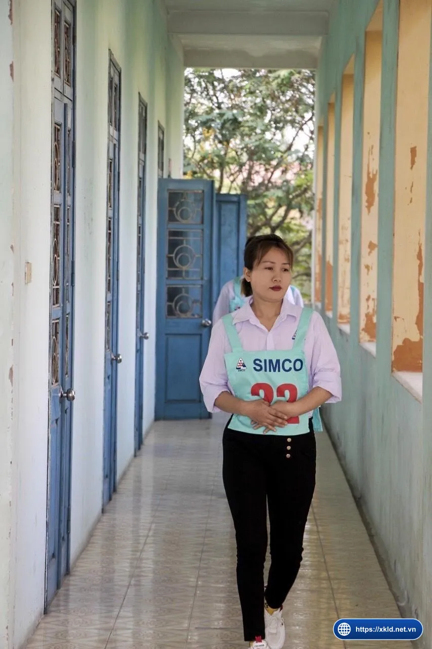 Một lao động nữ mặc yếm SIMCO Sông Đà số báo danh 22 đi trong hành lang, chụp lúc phỏng vấn đơn hàng
